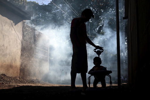 A man and his son stand outside their house while a health ministry worker fumigates in Managua