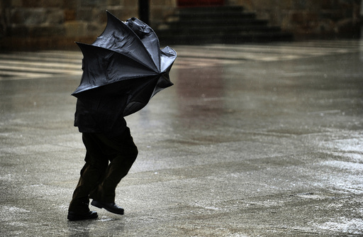 A man tries to hold his umbrella in the midst of strong gusts of wind in Gijon
