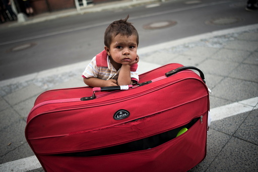 Migrant boy waits at his parents' suitcase as they leave the Berlin State Office for Health and Social Affairs with other newly arrived refugees who waited all day to apply for asylum in Berlin