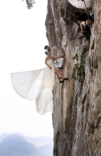 Fang Jing in a wedding gown and her husband, surnamed Zhao, pose for photographs as they hang from a cliff during a rock climbing exercise in Liuzhou