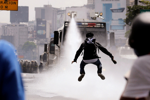 A demonstrator jumps away from a jet of water released from a riot security forces vehicle during a rally against Venezuela's President Nicolas Maduro in Caracas