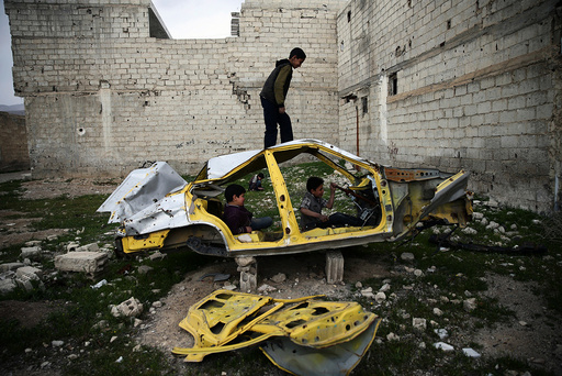 Boys play on a wrecked car in the rebel held besieged Douma neighbourhood of Damascus
