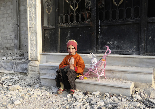 A girl carrying a doll sits on a step of a building as a boy peeks out from its gate in the Damascus suburbs of Arbeen