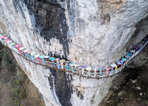 Women wearing cheongsam pose for pictures on a walkway along a cliff during an event in Chongqing Municipality