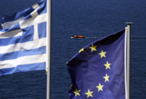 A dinghy overcrowded by migrants and refugees approaches the island of Lesbos as Greek and EU flags flutter atop a hill