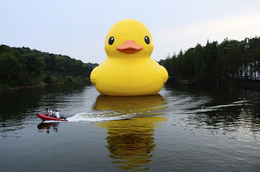 Workers travel on a speed boat past an inflatable Rubber Duck installation by Dutch artist Florentijn Hofman, on a lake of a botanic garden in Changsha