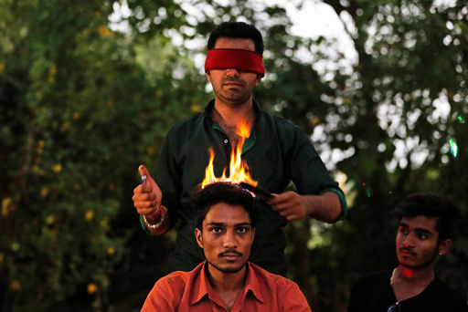 Vishnu Limbachiya, a hair artist, styles the hair of a man while wearing a blindfold at a park in Ahmedabad