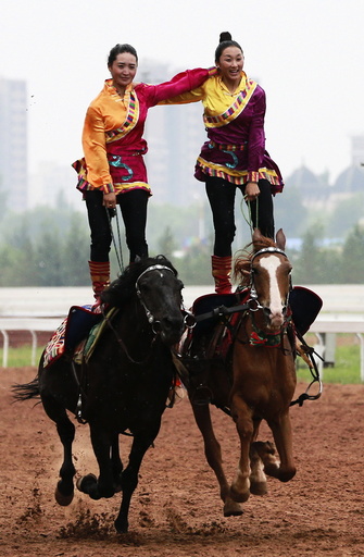 Tibetan women stand on their horses as they give an equestrian performance during the 10th Chinese Traditional Games of Ethnic Nationalities in Erdos