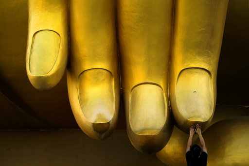 A woman prays while touching the fingers of a Buddha statue during the annual Makha Bucha Day, which celebrates Buddha's teachings, in Ang Thong