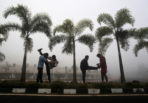 Men stretch during their routine exercises on a road divider during a foggy morning in Agartala