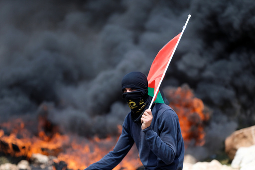 Protester holds a Palestinian flag as smoke rises from burning tyres during clashes with Israeli troops at a protest against Jewish settlements, in al-Mughayyir village near the West Bank city of Ramallah