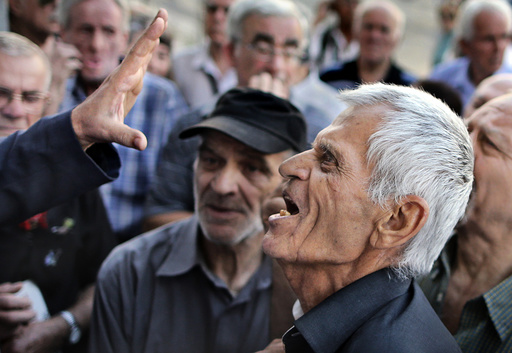 A pensioner argues with an official as he tries to enter a National Bank branch to receive part of his pension in Athens