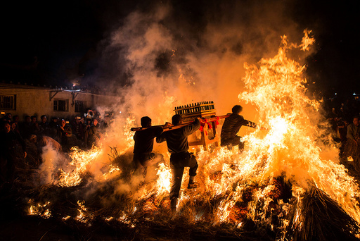 Men carrying a shrine jump over a bon fire, which means a wish for good luck during a traditional Chinese lunar new year celebration in Jieyang