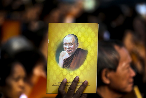 Man holds up a picture of Thailand's Supreme Patriarch, Somdet Phra Nyanasamvara Somdet Phra Sangharaja, as he takes part in a cremation ceremony in Bangkok
