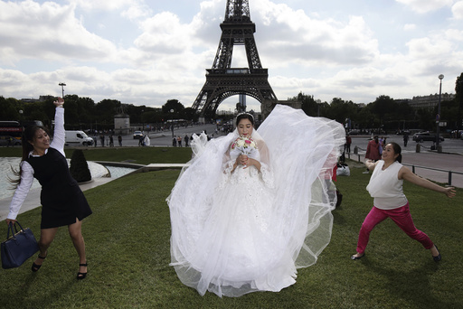 A Chinese future bride has her friends playing with her dress during a pre-wedding photoshoot in front of the Eiffel tower in Paris