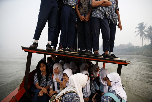 Students stand on the roof of a wooden boat as haze blankets the Musi River while they travel to school in Palembang