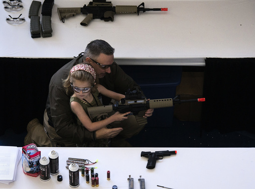 A man shows a girl how to hold an airsoft gun during the NRA Youth Day at the National Rifle Association's annual meeting in Houston, Texas