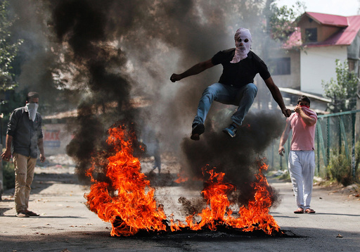 A man in a balaclava jumps over burning debris during a protest against the recent killings in Kashmir, in Srinagar