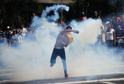 A demonstrator throws back a tear gas canister during clashes with security forces at an opposition rally in Caracas