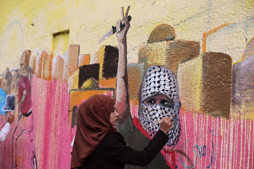Palestinian woman paints a mural, depicting a masked Palestinian holding a knife, in support of Palestinians committing stabbing attacks against Israelis, in Rafah in the southern Gaza Strip