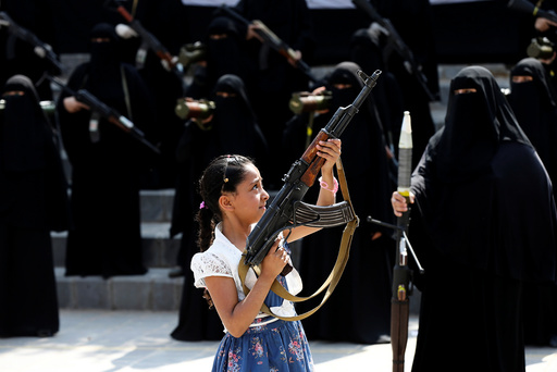 Girl holds a rifle in front of women loyal to the Houthi movement taking part in a parade to show support to the movement in Sanaa, Yemen