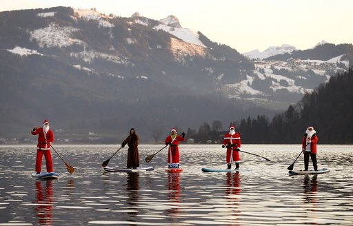 People dressed as Santa Claus pose on their stand-up paddles as they cross Lake Aegerisee near Oberaegeri