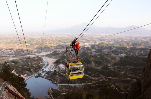 A staff of Shiniuzhai scenic zone dressed as Santa Claus stands on top of a cable car to send gifts to visitors, in Pingjiang