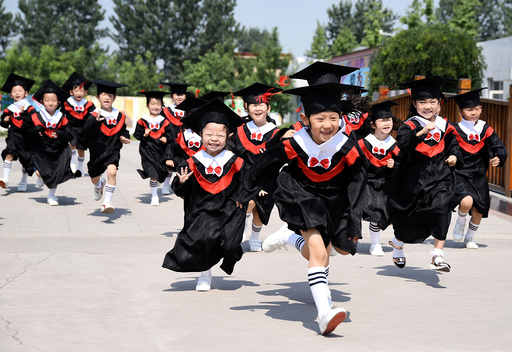 Children in gowns and mortarboards run with smiles during their kindergarten graduation ceremony in a kindergarten in Handan