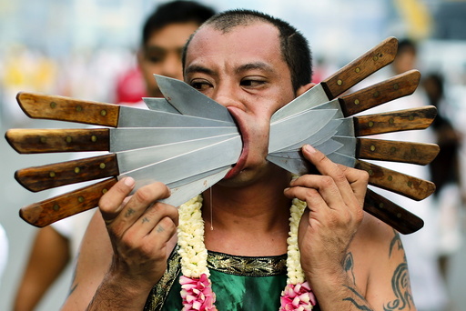 A devotee of the Chinese Samkong Shrine walks with knives pierced through his cheeks during a procession celebrating the annual vegetarian festival in Phuket
