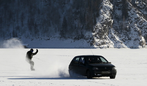 Car tows snowboarder along frozen surface of Yenisei River in Taiga district outside Krasnoyarsk