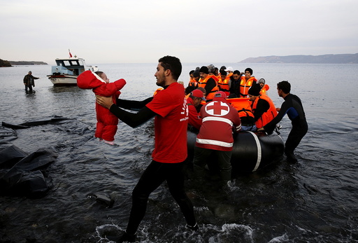 A Red Cross volunteer carries a refugee baby at a beach on the Greek island of Lesbos