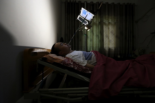 Xu, suffering from physical disability after a severe spine injury, uses an extended stylus to type on a tablet as he runs his online store on his bed, in Houwu village of Quzhou