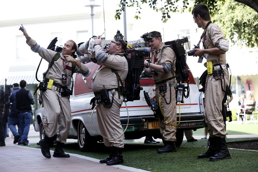 Enthusiasts wearing Ghostbusters costumes stand by an ECTO-1, the vehicle used in the upcoming movie 