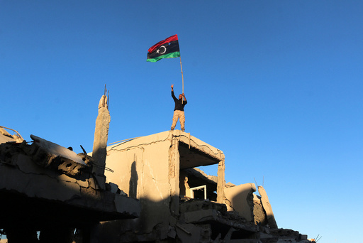 Fighter of Libyan forces waving a Libyan flag flashes victory sign as he stands atop the ruins of a house after forces finished clearing Ghiza Bahriya, the final district of the former Islamic State stronghold of Sirte