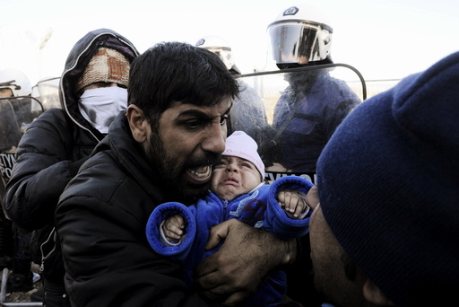 A stranded migrant holding a baby shouts next to a Greek police cordon following scuffles at the Greek-Macedonian border, near the village of Idomeni