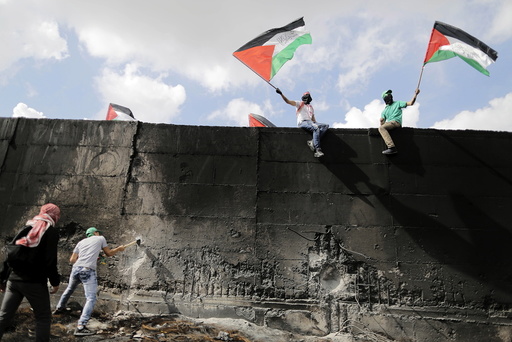 Palestinian protester tries to hammer a hole through the Israeli barrier that separates the West Bank town of Abu Dis from Jerusalem, as others wave Palestinian flags during clashes with Israeli troops