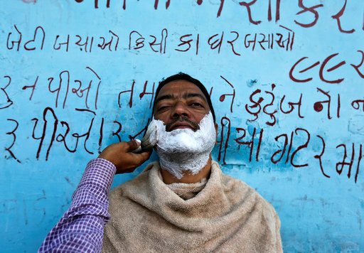 A man gets a shave from a roadside barber in Ahmedabad
