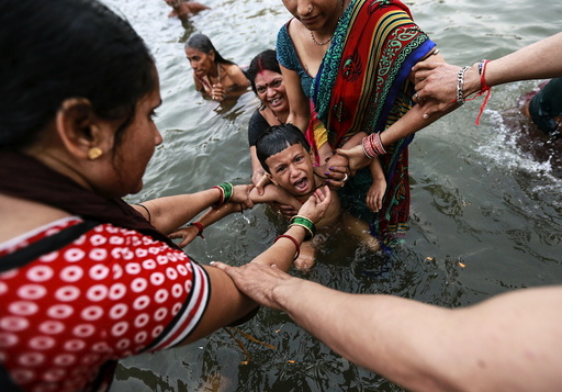 A boy cries as he is dipped by his relatives in the Godavari river during 