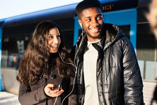 Happy young friends listening music through hands-free device against train