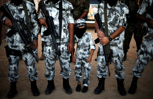 A Palestinian boy stands between militants of the Popular Resistance Committees during a military parade in Rafah