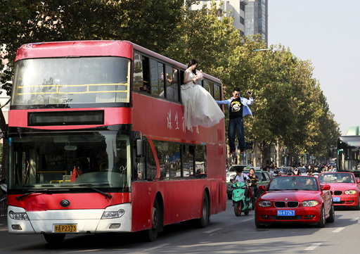 Magician Lei is seen suspended outside a double-deck bus, next to a woman in a wedding gown, as they participate in a performance on a street in Zhengzhou