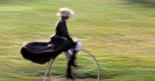 A participant wearing historical costume rides her high-wheel bicycle before the annual penny farthing race in Prague