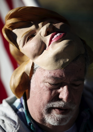 Protester Bob Kunst reads political literature while taking a break from wearing a Hillary Clinton mask outside the Fox Business News Republican Presidential Debate at the North Charleston Coliseum in North Charleston