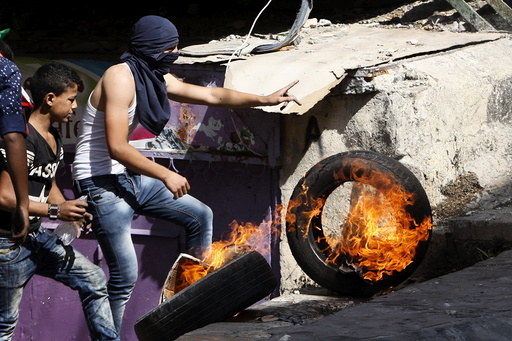 Palestinian pushes a burning tyre during clashes with Israeli troops in the occupied West Bank city of Hebron