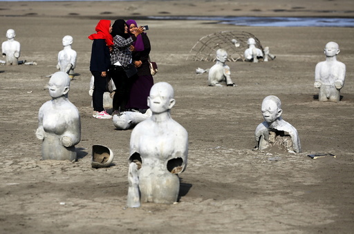 Women take pictures between stone sculptures of half-buried people at the Lapindo mud field in Sidoarjo