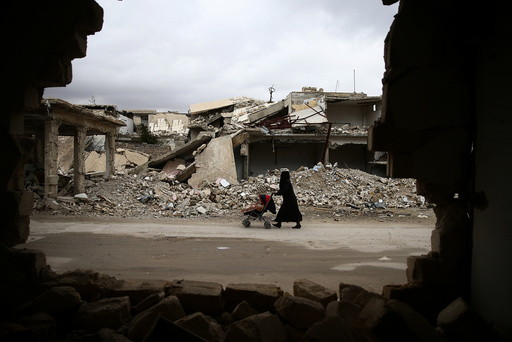 A woman pushes a baby trolley past damaged buildings in the rebel held besieged city of Douma