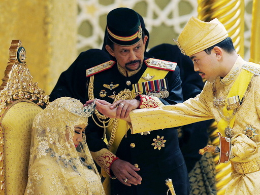 Brunei's Sultan Hassanal Bolkiah holds the arm of his son Prince Abdul Malik to bless Malik's new wife Dayangku Raabi'atul 'Adawiyyah Pengiran Haji Bolkiah during the enthronement ceremony at their wedding in Bandar Seri Begawan