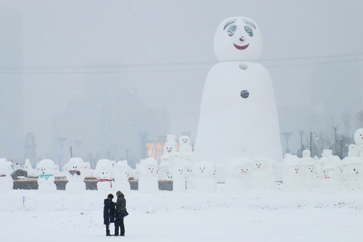 People are seen next to a giant snowman at a park in Harbin