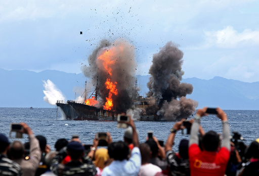People take pictures of a burning ship as the government destroyed foreign boats at Morela village in Ambon island