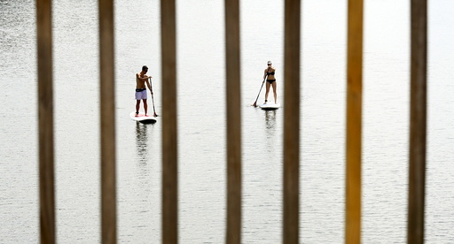 A couple, seen through a bridge railings, beat the heat by taking to the water to paddle board along the Potomac River in Washington